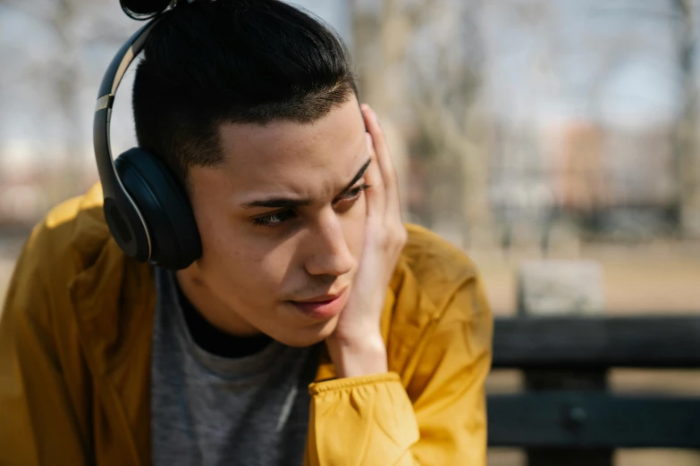 a young man sitting on a bench wearing headphones, trending on pexels, realism, non-binary, with a hurt expression, hispanic, tinnitus