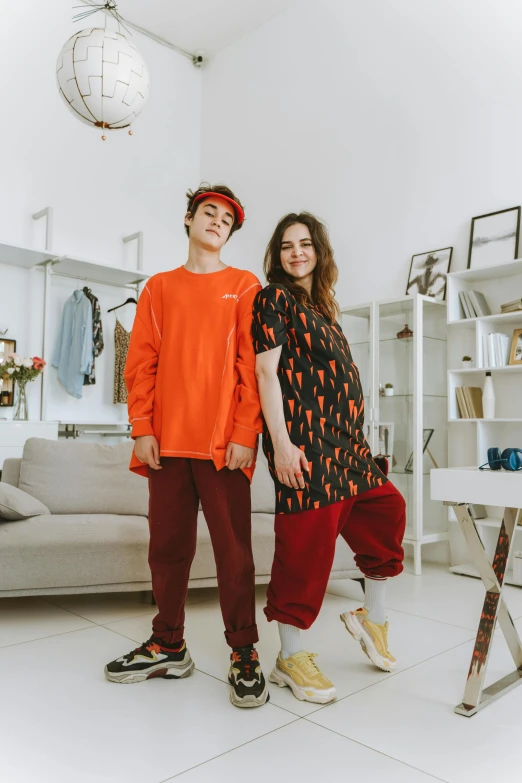 two people standing next to each other in a living room, by Julia Pishtar, trending on pexels, antipodeans, she is wearing streetwear, red and orange colored, teenage boy, baggy pants