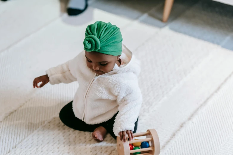 a baby in a green turban playing with a wooden toy, by Emma Andijewska, pexels contest winner, black young woman, sitting down casually, gif, top down photo