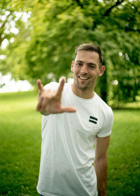 a man standing on top of a lush green field, a photo, inspired by Adrian Zingg, happening, with index finger, smiling male, at a park, wearing a black t-shirt