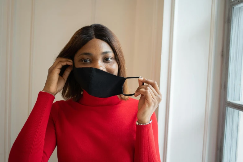 a woman wearing a face mask in front of a window, trending on pexels, black and red silk clothing, wearing a black sweater, aida muluneh, rounded face