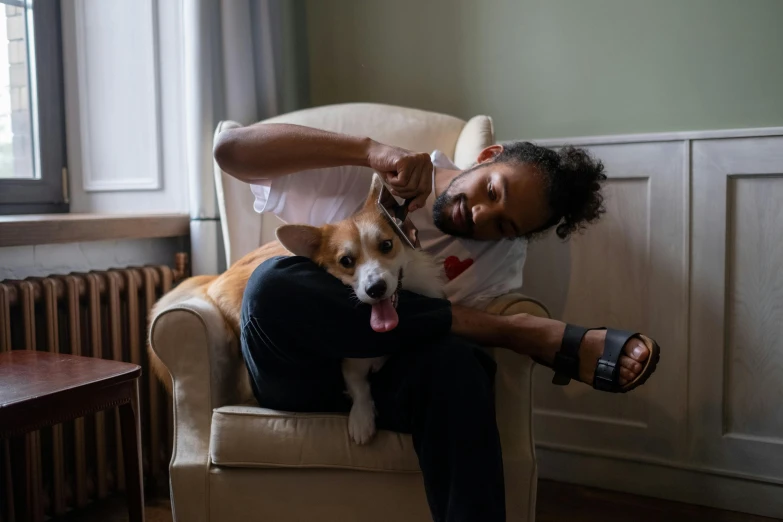 a man sitting in a chair with a dog on his lap, pexels contest winner, corgi, : kendrick lamar, fan favorite, at home