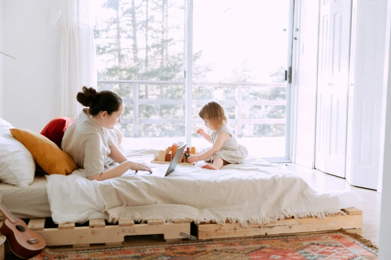 a woman sitting on top of a bed next to a little girl, pallet, canva, full device, large windows