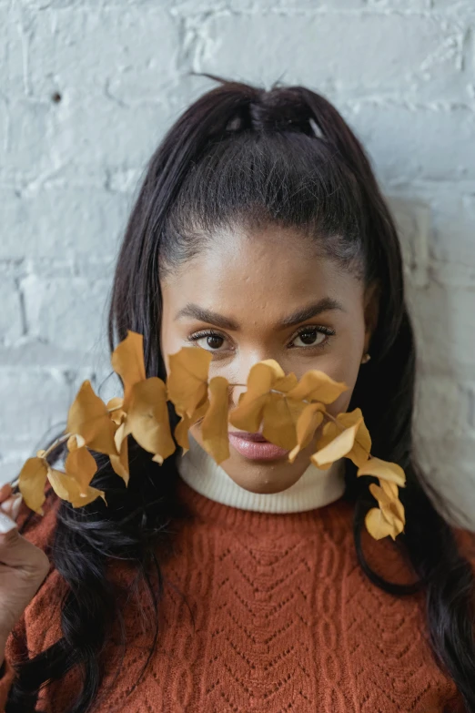 a woman holding leaves in front of her face, trending on pexels, renaissance, he is wearing a brown sweater, tessa thompson inspired, with a ponytail, stylized photo