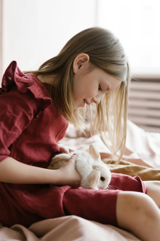 a little girl sitting on top of a bed holding a white cat, pexels, rabbits, brown, velvet, pink