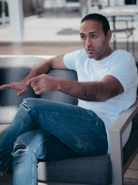 a man sitting on a couch pointing at something, inspired by Dimitre Manassiev Mehandjiysky, pexels contest winner, les nabis, wearing jeans, dressed in a white t shirt, looking off to the side, tom morello