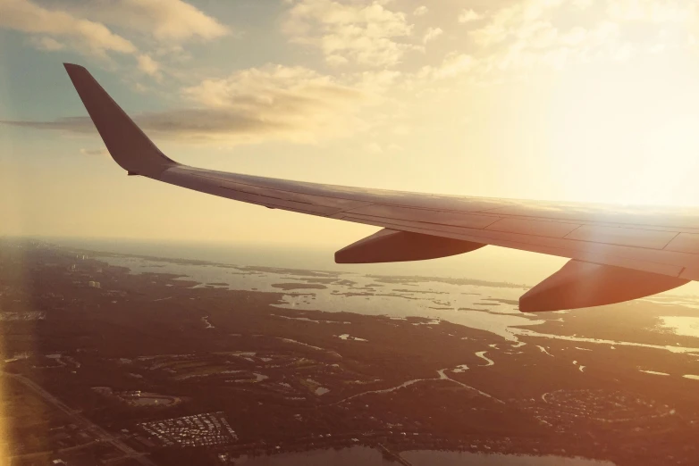 the wing of an airplane flying over a body of water, pexels contest winner, modernism, sunset light, vintage style, travel ad, 'wherever you go