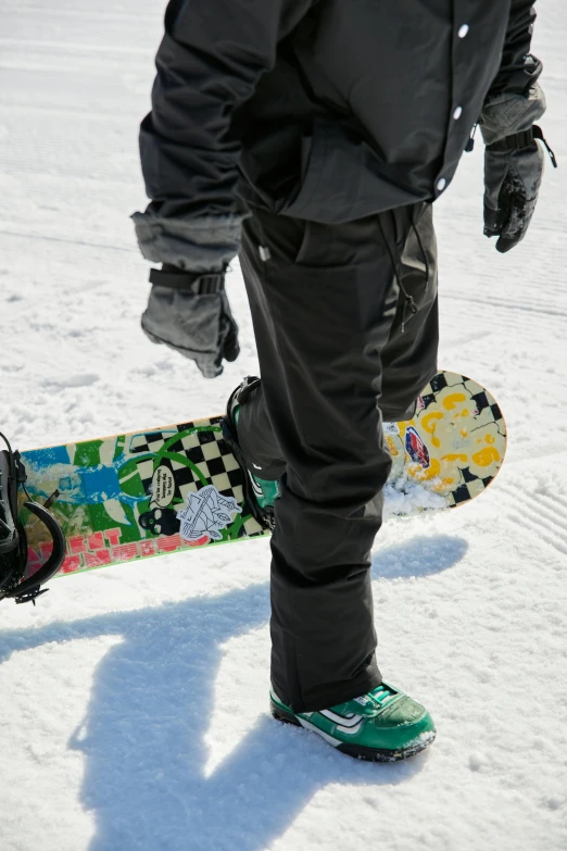 a person standing in the snow holding a snowboard, wearing pants, zoomed in, wearing gloves, pants
