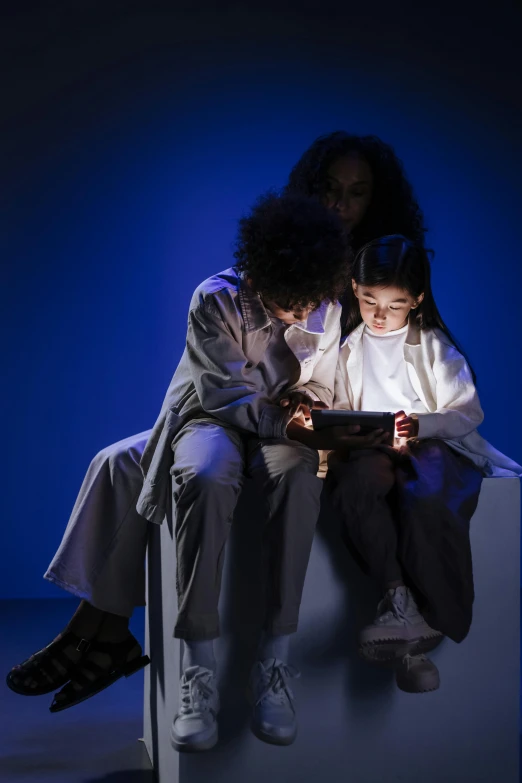 a couple of people sitting next to each other on a bench, by Alison Geissler, interactive art, using a magical tablet, 3 actors on stage, children, neutral light