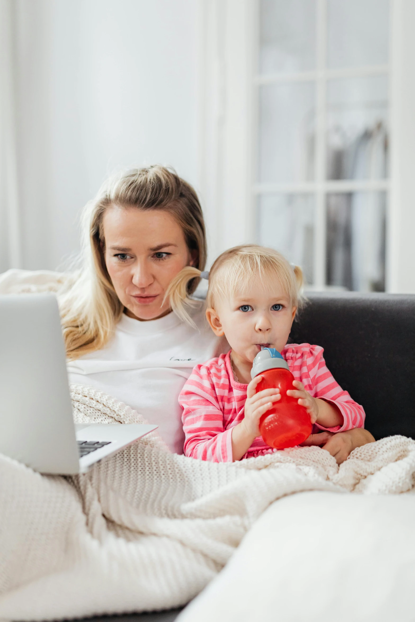 a woman sitting on a couch with a baby and a laptop, looking distracted, square, snacks, high-quality photo