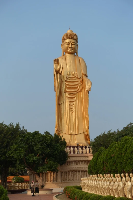 a large golden statue sitting on top of a lush green field, from china, viewed from the harbor, wooden statue, facing front