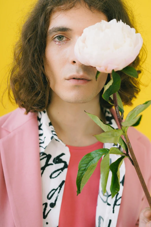 a man holding a flower in front of his face, an album cover, trending on pexels, aestheticism, pink clothes, portrait of timothee chalamet, lizard king / queen forgiveing, pastel'