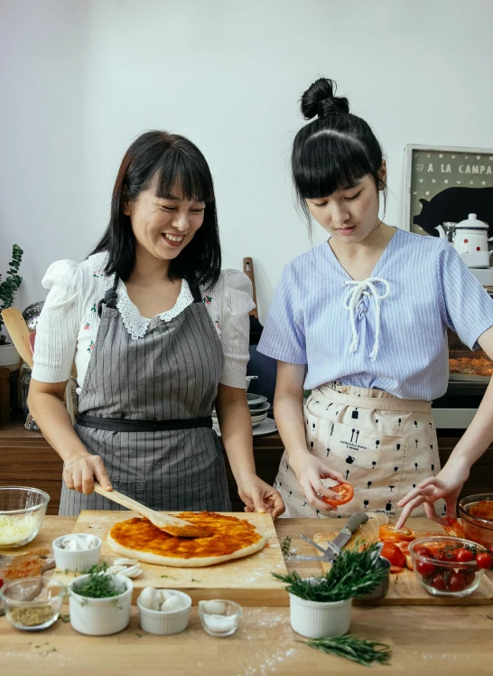 two women in aprons preparing food on a table, inspired by Yukimasa Ida, pexels contest winner, cooking pizza, square, full body image, huang yuxing and aya takano