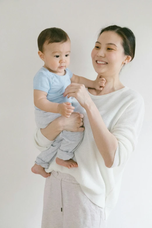 a woman holding a baby in her arms, inspired by Li Di, unsplash, minimalism, wearing a light blue shirt, japanese collection product, ivory, wearing pajamas