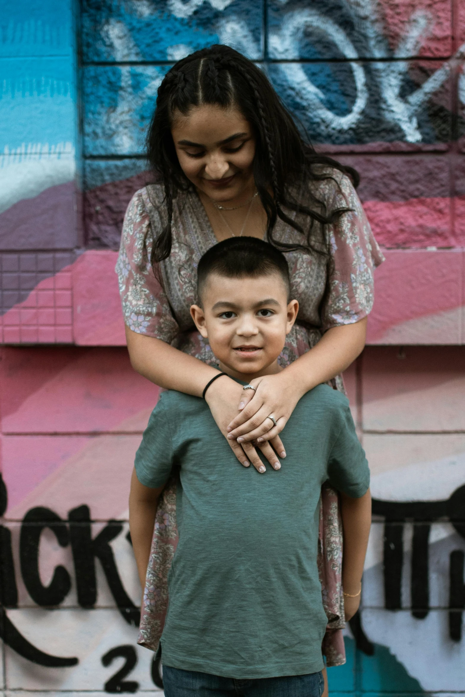 a woman standing next to a boy on a skateboard, a portrait, pexels contest winner, graffiti, arm around her neck, alanis guillen, square, stacked image