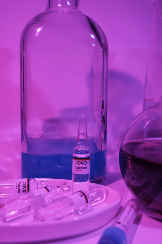 a glass bottle sitting on top of a table next to a glass filled with liquid, by Jeanna bauck, syringes, purple and blue neons, covid, clone laboratory