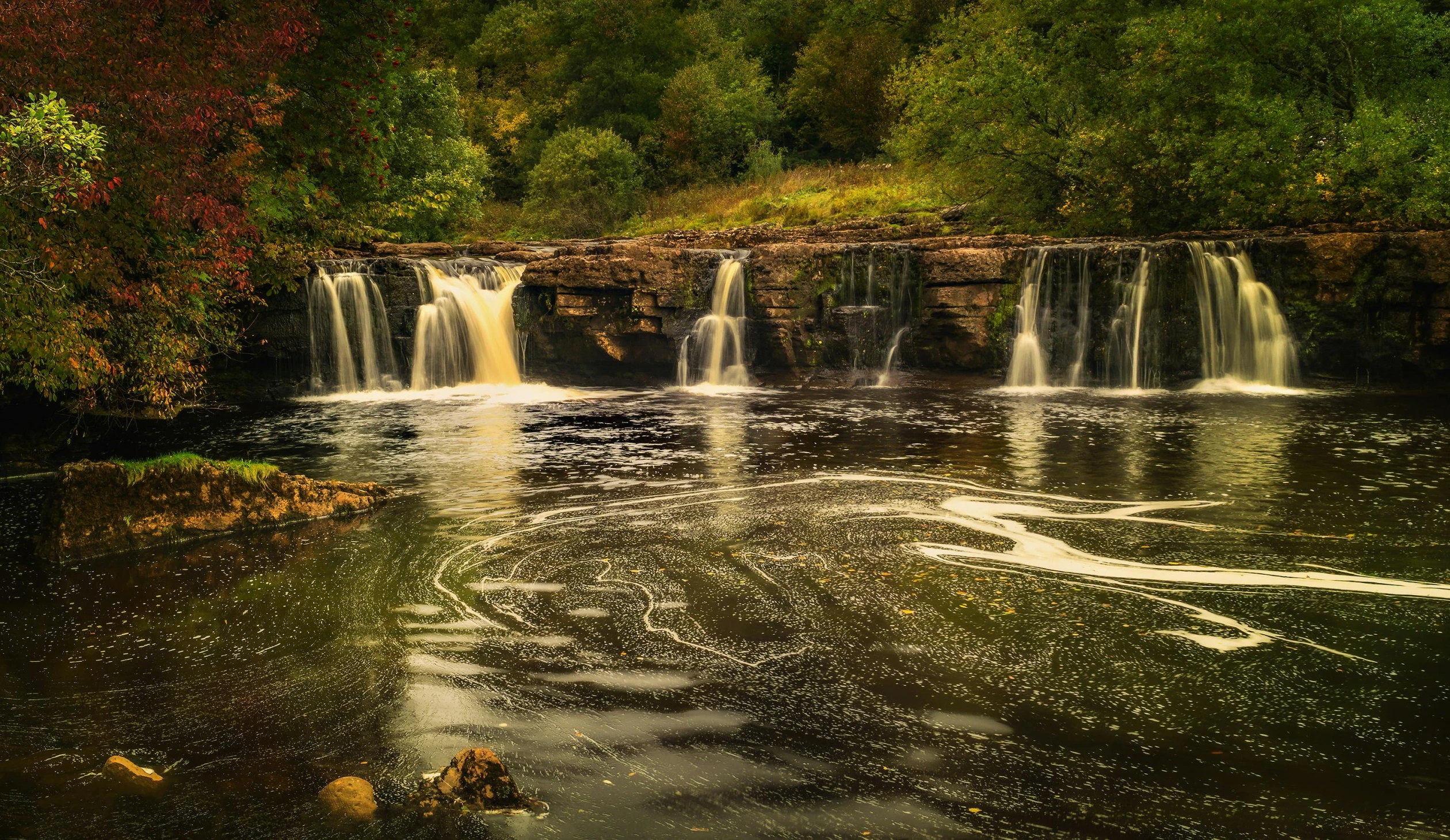 a large waterfall in the middle of a forest, by Andrew Allan, reflections on the river, sandfalls, multiple waterfalls, landscape photo