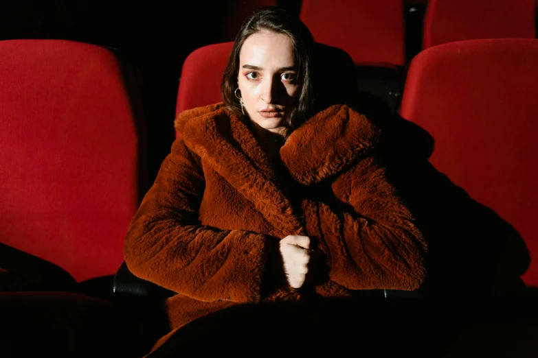 a woman sitting in a red chair in a movie theater, an album cover, pexels contest winner, antipodeans, pelt coats, dilraba dilmurat, cinematic outfit photo, brown tuffle coat