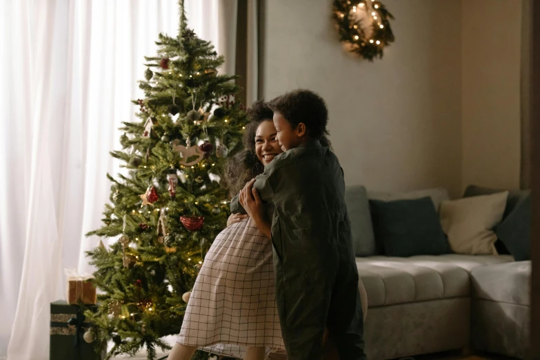 two women hugging each other in front of a christmas tree, pexels contest winner, happening, husband wife and son, avatar image, hugging her knees, diverse