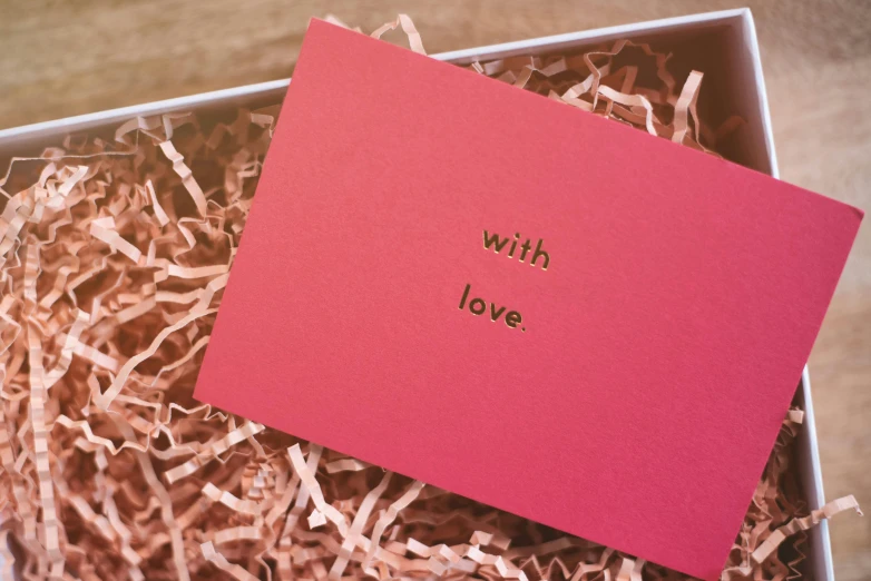 a pink box sitting on top of a pile of shredded paper, by Julia Pishtar, pexels contest winner, romanticism, with some hand written letters, alec soth : : love, whole card, gold embroidery