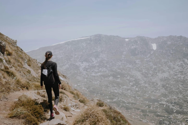 a woman walking up the side of a mountain, pexels contest winner, miranda meeks, facing away from camera, eng kilian, high above treeline