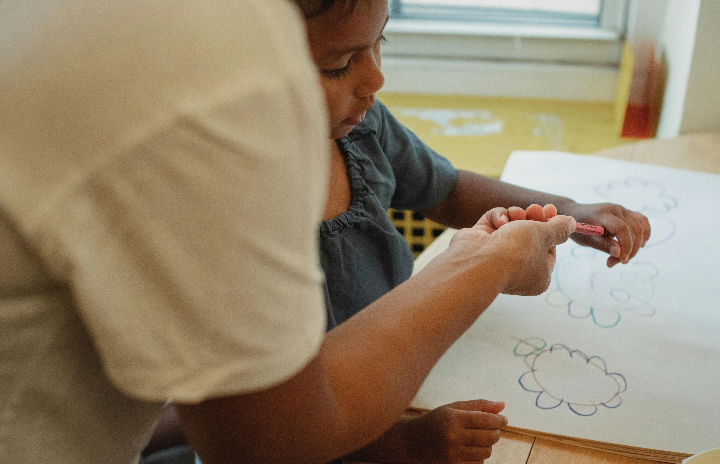 a woman helping a child draw on a piece of paper, by Arabella Rankin, pexels contest winner, back of hand on the table, whiteboards, photo of a black woman, subtle detailing