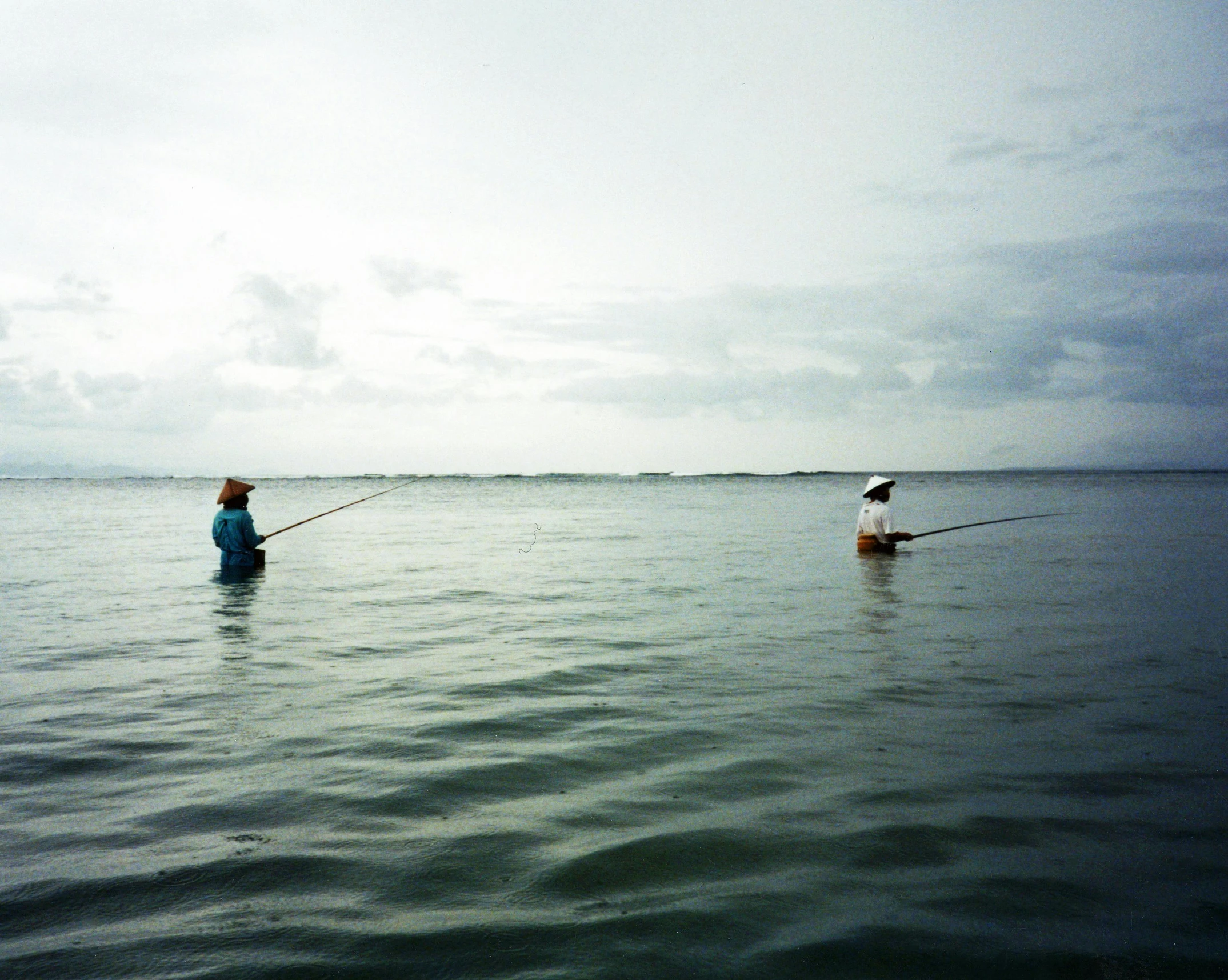 a couple of people that are standing in the water, by Carey Morris, hurufiyya, fishing, photo taken on fujifilm superia, low horizon, waiting to strike