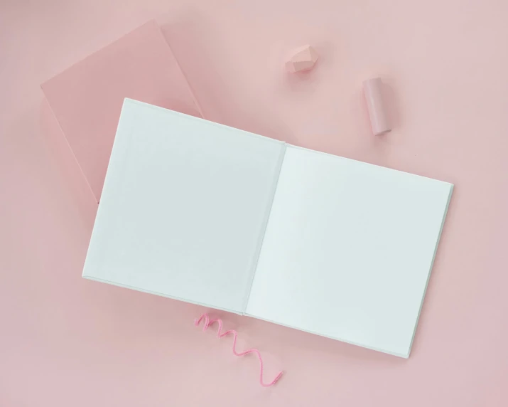 an open book sitting on top of a pink surface, album, square shapes, white sheets, no text
