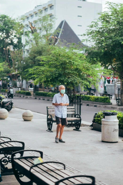 a man walking down a sidewalk next to park benches, arsitektur nusantara, old man doing with mask, open street maps, full body image