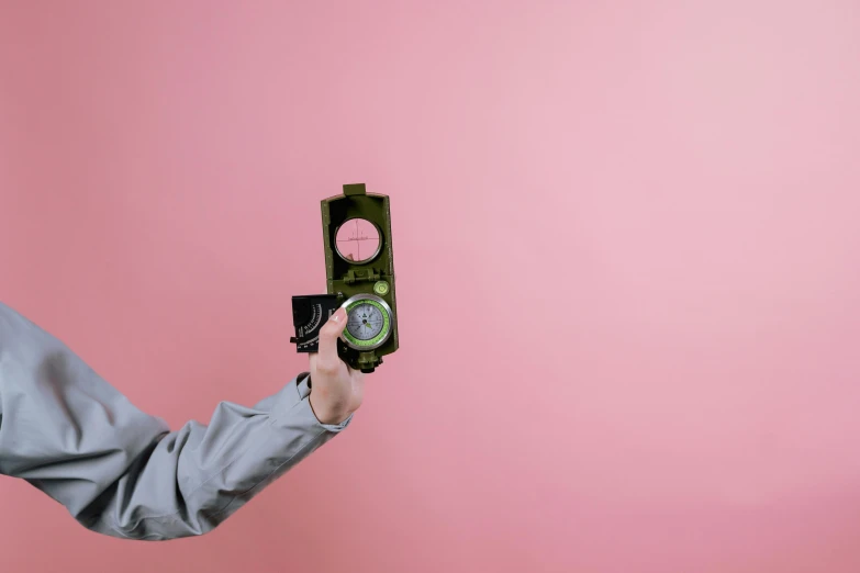 a close up of a person holding a camera, inspired by Wes Anderson, visual art, green and pink colour palette, military photography, compass, pink