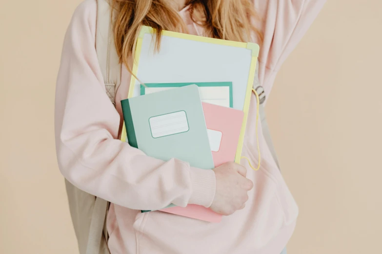 a woman in a pink sweatshirt holding a bunch of folders, by Nicolette Macnamara, trending on pexels, academic art, dressed as schoolgirl, pale pastel colours, notebook, background image