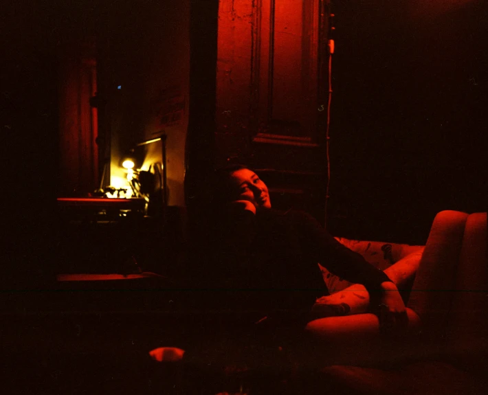 a person sitting on a couch in a dark room, inspired by Nan Goldin, red flames, 35 mm photo