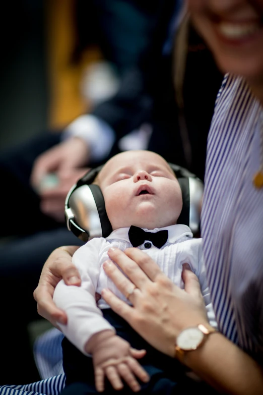 a woman holding a baby wearing headphones, by Nina Hamnett, happening, holy ceremony, wearing a tuxedo, lachlan bailey, resting