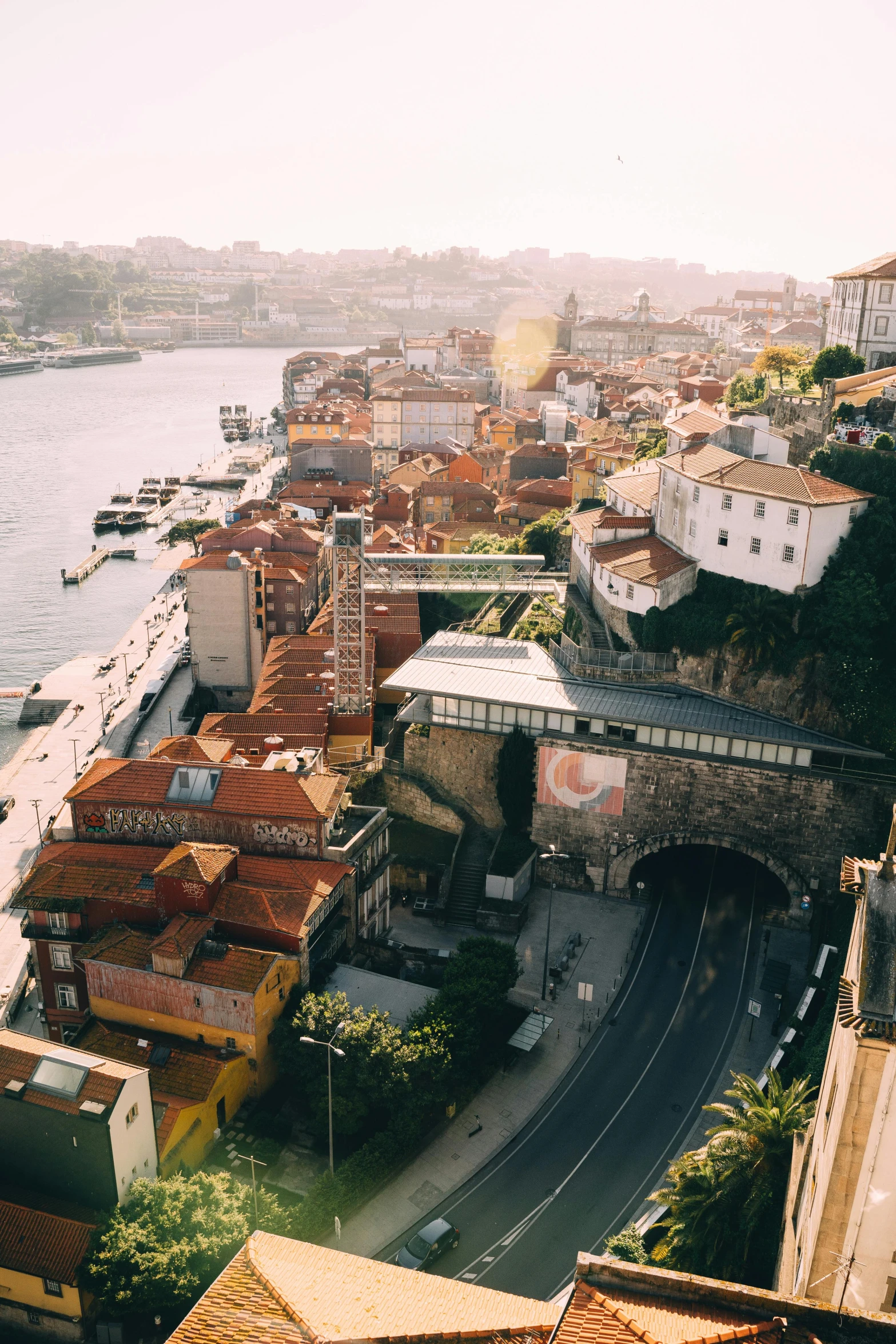 a view of a city from the top of a building, river flowing through a wall, gui guimaraes, sunfaded, curved bridge