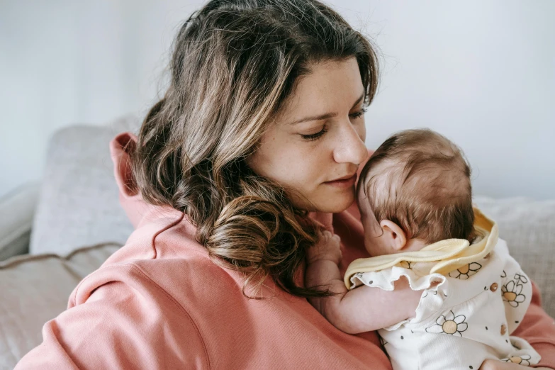 a woman sitting on a couch holding a baby, pexels, manuka, medium head to shoulder shot, thumbnail, brunette