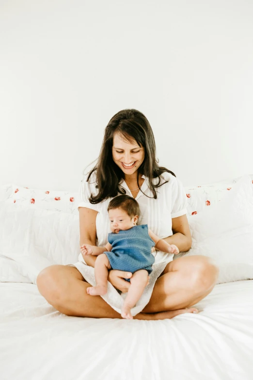 a woman sitting on a bed holding a baby, profile image, denim, small, small features