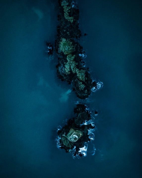 a small island in the middle of a body of water, by Jesper Knudsen, unsplash contest winner, hurufiyya, deep dark sea, bird\'s eye view, rock formations, blue glow