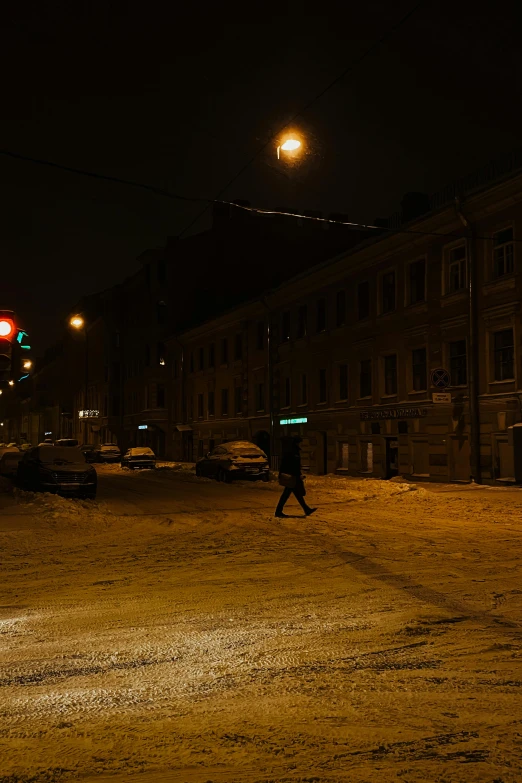 a person walking across a snow covered street at night, in russia, empty streetscapes, low light, dusty street