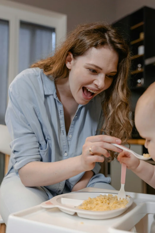 a woman feeding a baby in a high chair, pexels contest winner, art & language, all overly excited, drinking cough syrup, confident looking, playful smile