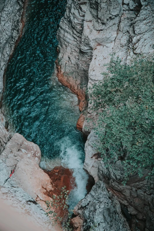 a man standing on top of a cliff next to a river, by Jacob Toorenvliet, pexels contest winner, teal and orange colour palette, top down view, small waterfall, swinging on a vine over a chasm