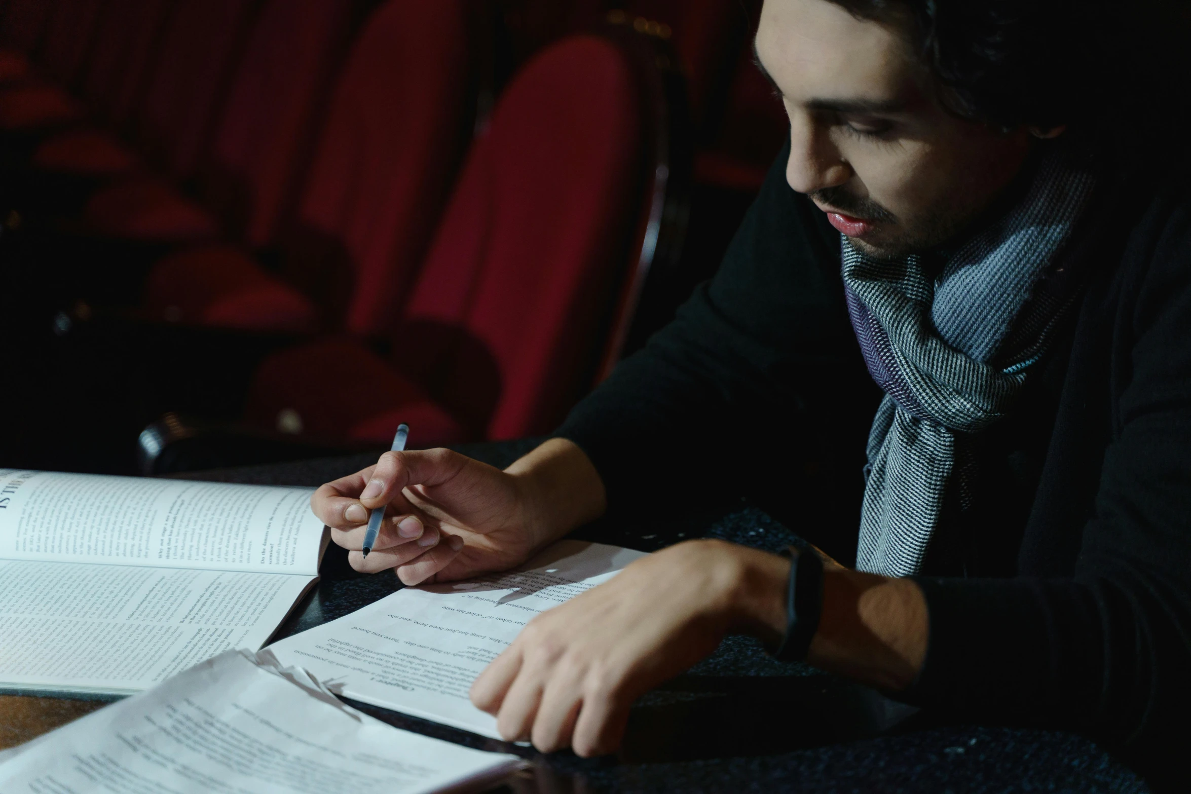 a man sitting at a table reading a book, in a cinema, pen and paper, sam nassour, student