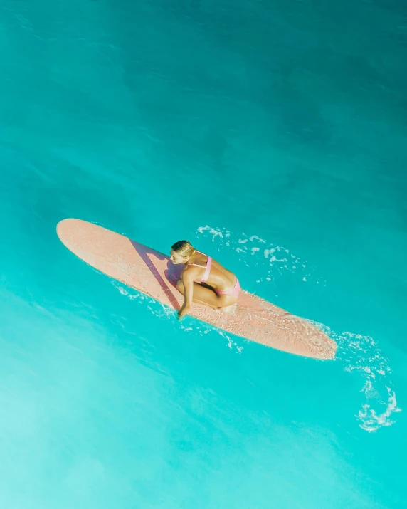 a woman riding a surfboard on top of a body of water, from above, brown and cyan color scheme, thumbnail, sunbathed skin