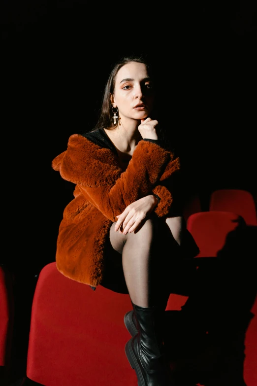 a woman sitting on top of a red chair, inspired by Elsa Bleda, instagram, baroque, wearing a fur coat, [ theatrical ], dilraba dilmurat, black and orange