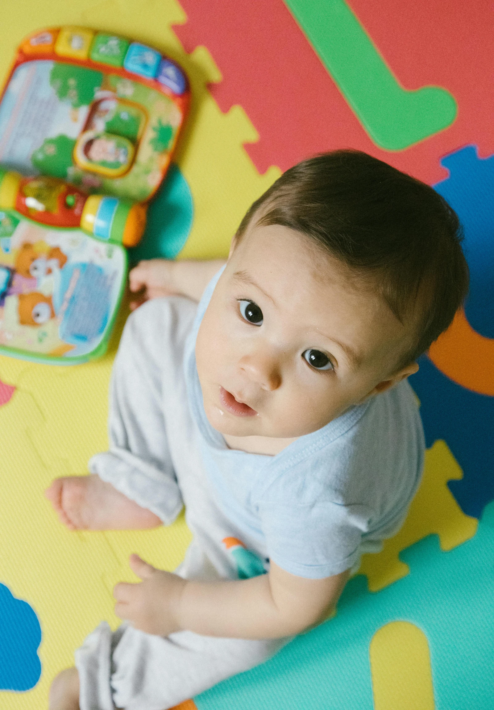 a baby laying on the floor next to a toy phone, pexels contest winner, figuration libre, looking serious, multicolored, gif, boy with neutral face