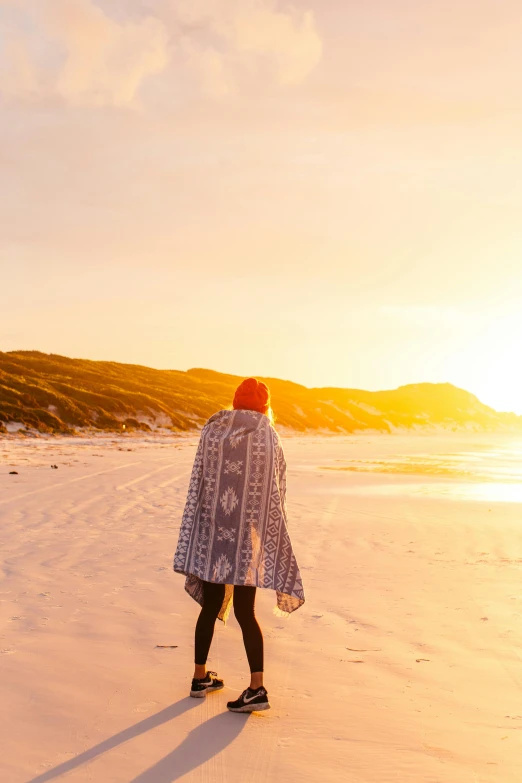 a person walking on a beach at sunset, covered with blanket, australian beach, looking off to the side, cape