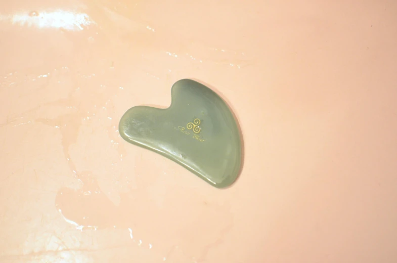 a green heart shaped object on a pink surface, inspired by Jean Arp, trending on pexels, hurufiyya, grey facial flesh, lie on a golden stone, skincare, silicone cover