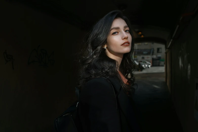 a woman standing next to a wall with graffiti on it, pexels contest winner, photorealism, long wavy dark hair, a man wearing a black jacket, with a backpack, ( low key light )