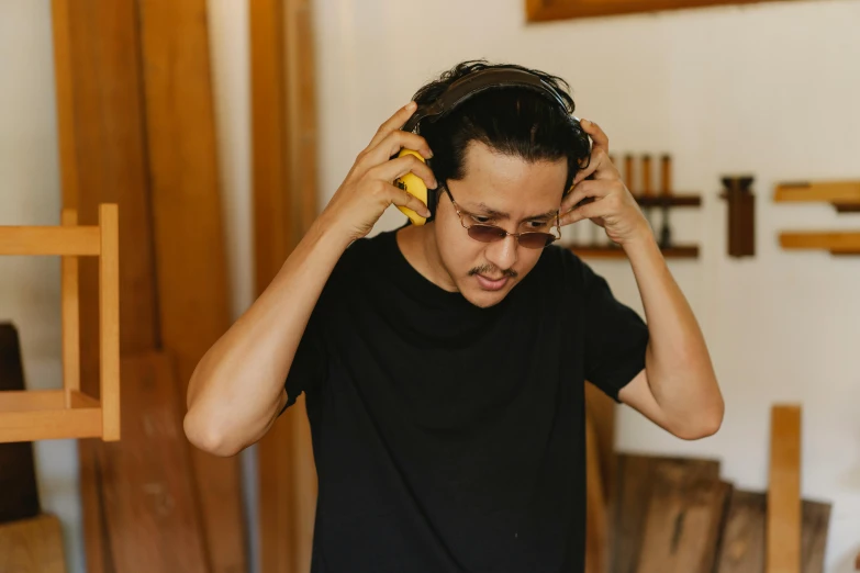 a man holding a pair of headphones on top of his head, trending on pexels, process art, wearing gold glasses, asian male, thumbnail, wood headphones