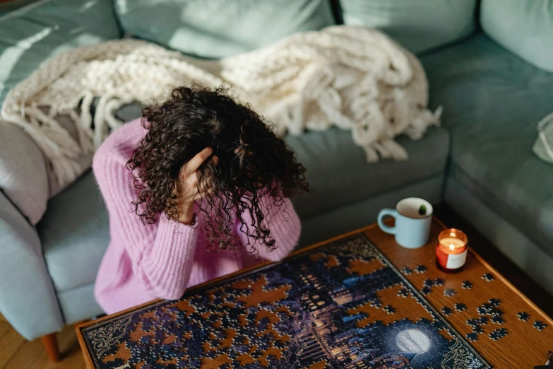 a woman sitting on a couch in a living room, a jigsaw puzzle, by Julia Pishtar, trending on pexels, messy hair bedhead, cozy candlelight, frustrated detailed, board games on a table