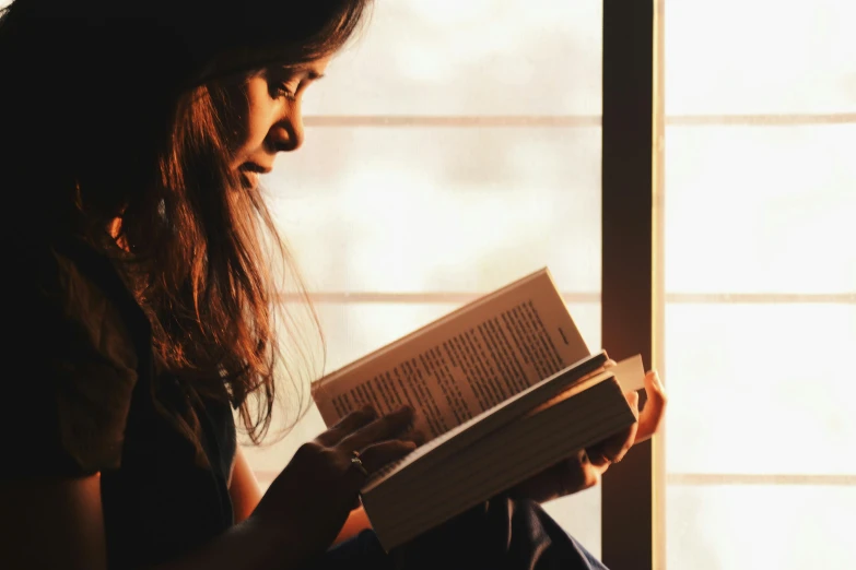 a woman sitting on a window sill reading a book, pexels contest winner, glowy light, reading engineering book, open books, with backlight